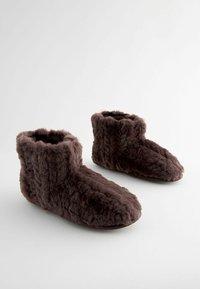 Braune, flauschige Hausschuhe aus weichem Material mit mittelhohem Design und abgerundeten Zehen. Texturierte Außenseite mit gemütlichem Erscheinungsbild.