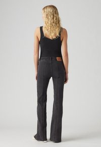 Black flared jeans with prominent stitching, high waist, and textured fabric. Features a branded leather patch on the back.