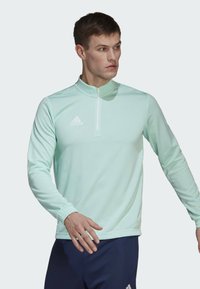 Mintgrünes, langärmliges Sportoberteil mit einem Viertelreißverschluss-Design, das ein weißes Adidas-Logo auf der linken Brust und gerippte Bündchenakzente aufweist.