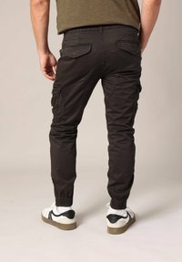 Zwarte cargobroek met elastische boorden, achterzakken en zijzakken. Draagt witte sneakers met zwarte accenten.