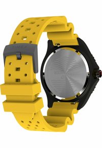 Montre Timex avec un boîtier noir, un cadran rond argenté, et un bracelet en silicone jaune texturé avec des découpes rectangulaires et une boucle grise.