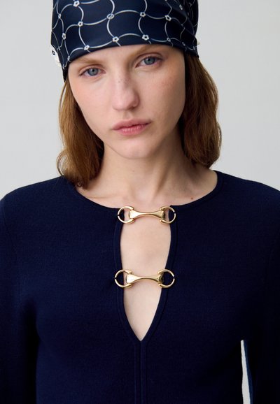 Maglione lavorato a maglia blu navy con scollatura a V profonda, dotato di due chiusure con bottone a leva dorato sul petto. Texture liscia, maniche lunghe e design minimal.