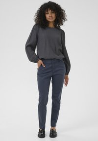 Dark gray textured blouse with long sleeves paired with slim-fit navy trousers and black loafers. Simple, streamlined design with minimal accents.