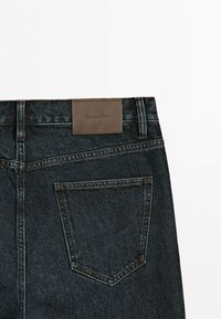 Bagsiden af mørkeblå denimjeans med en enkelt baglomme og en brun læderlap med teksten "Massimo Dutti" på taljen.