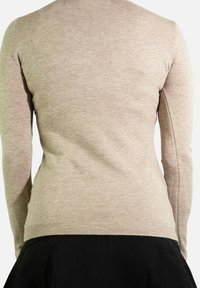 Pull à manches longues beige avec un col et des poignets côtelés, présentant une texture lisse et une coupe ajustée, associé à une jupe noire.