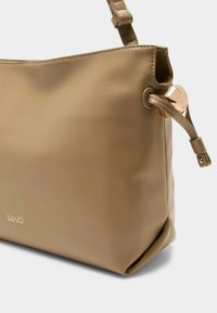 Borsa a mano in pelle beige con una texture liscia, caratterizzata da un dettaglio decorativo in metallo e una cinghia cucita. Logo stampato sul lato.