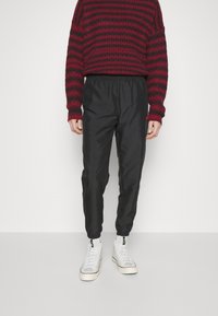 Black, lightweight, elastic-waist pants with cuffed ankles paired with a red and black striped knit sweater and white high-top sneakers.