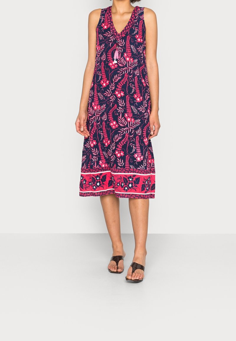 Robe sans manches bleu marine ornée de motifs floraux et de feuilles roses, avec un décolleté en V et un ourlet accentué par des bordures à motifs.