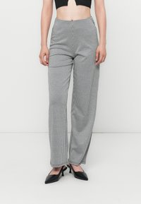 Pantalons à motif pied-de-coq noir et blanc avec taille haute, coupe large et texture lisse. Associés à des chaussures noires à bouts pointus.