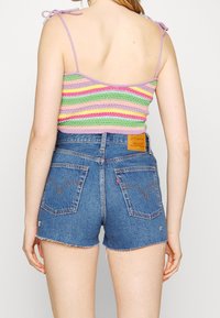 Barevný háčkovaný crop top s levandulovými ramínky, v kombinaci s tmavě modrými džíny s vysokým pasem, které mají třepené lemy a zadní kapsy.