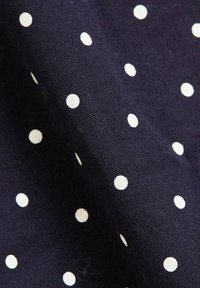Tissu bleu foncé avec de petits pois blancs régulièrement espacés et une texture tissée visible, légèrement plié pour montrer la profondeur.
