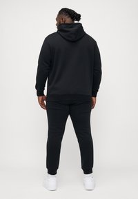 Schwarzer Kapuzenpullover und passende Jogginghose aus weichem Stoff. Der Kapuzenpullover hat eine Kängurutasche und eine verstellbare Kordel; die Jogginghose hat gerippte Bündchen.