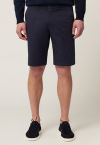 Navyblauwe katoenen korte broek met een platte voorkant, zijzakken en een klassieke pasvorm, gecombineerd met zwarte leren schoenen en een donkere trui.