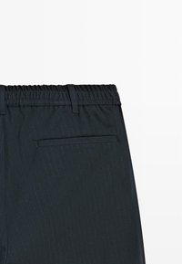 Pantaloni neri a righe sottili con vita elastica, dotati di una tasca posteriore e una texture liscia. Design sartoriale visibile.