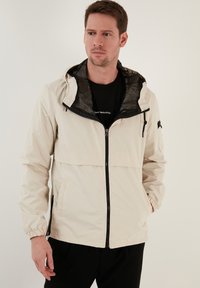 Lichtbeige windbreakerjack met een halve ritssluiting aan de voorkant, elastische manchetten en een gevoerde capuchon van mesh. Voorzien van een borstzak en zijzakken.