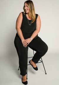 Zwarte jumpsuit met een mouwloos ontwerp, gladde stof en relaxte pasvorm. Benadrukt door een ronde ketting en gedragen met zwarte flats.