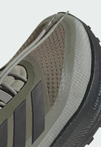 Hiking shoe with a textured brown and grey upper, featuring mesh panels, rubber sole, and gray laces. Notable three-stripe design on the side.