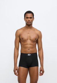 Boxer en coton noir à coupe ajustée, avec un logo blanc contrastant sur la ceinture élastique. Texture lisse et détails minimalistes.