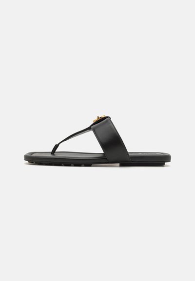 Sandale flip-flop noire à texture mate, avec une large sangle et un accent doré. La semelle est plate avec une texture antidérapante pour une meilleure adhérence.