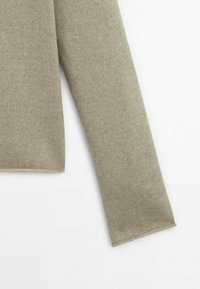 Manica di un maglione beige lavorato a maglia con una texture a coste, caratterizzata da un taglio diritto e orlo pulito. Il materiale appare morbido e caldo.