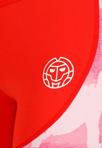 Top de bañador rojo con una textura suave, que presenta un logo blanco en forma de cara, y un tejido rosa con patrones en el borde.