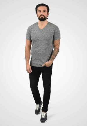 Sivi v-neck majica, kratki rukavi, prilagođenog kroja, uparena s crnim trapericama i sivim tenisicama s bijelim detaljima i vezicama.