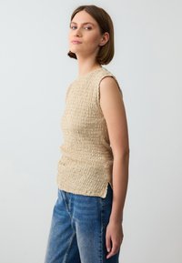 Beige gebreide top met textuur, zonder mouwen en zijsplitten, gecombineerd met casual blauwe denim jeans. Eenvoudige, relaxte silhoutte.