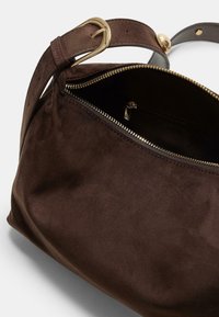 Braune Wildlederhandtasche mit goldfarbenem Rei�ßverschluss, verstellbarem Träger und Innenfach. Glatte Textur und weiche Form mit abgerundeten Kanten.