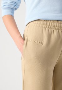Beiga sweatpants med elastisk midjeband, med en sidficka och präglad logotypdetalj. Slät, mjuk textur, modern design.