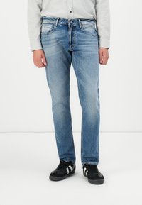 Jeans in denim azzurro chiaro con design classico a cinque tasche, taglio dritto, texture sbiadita e sottili dettagli di cucitura. Indossati con sneaker nere.