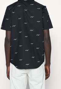 Zwart shirt met korte mouwen, gemaakt van gladde stof, met een herhalend wit scriptpatroon. De onderkant is gebogen, met een losse pasvorm.