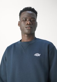 Felpa blu navy in tessuto texture, con scollo a costine e logo ricamato sul petto. Vestibilità rilassata, stile casual.