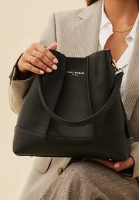 Black leather handbag with a smooth texture, curved top, and a gold logo. Features a single, rounded handle and contrasting seams.