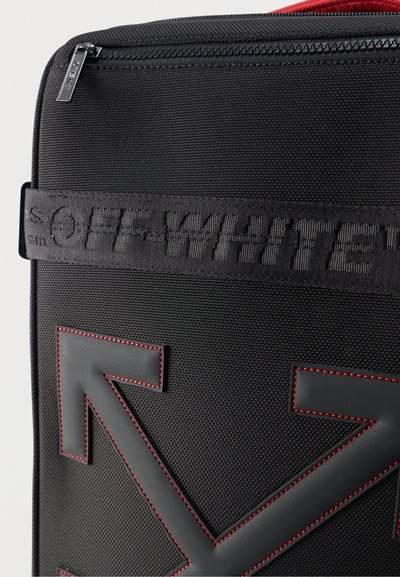 Μαύρο υφασμάτινο σακίδιο με δύο μεγάλες ραμμένες διασταυρωμένες βέλη με κόκκινο περίγραμμα και μαύρο λουράκι με ανάγλυφη την επιγραφή "OFF-WHITE".