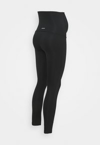 Leggings pretos de cintura alta feitos de tecido elástico. Apresentam uma textura suave, um design ajustado ao corpo e uma marcação discreta na cintura.