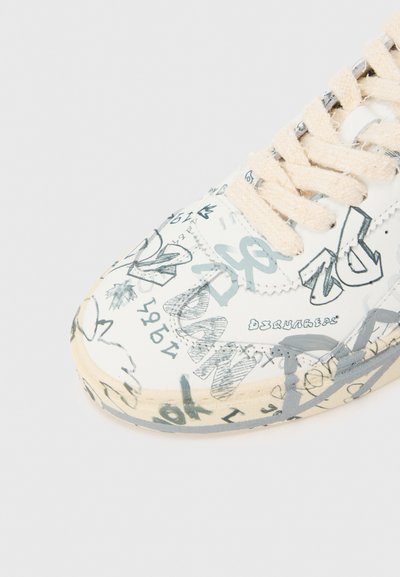 Λευκό αθλητικό παπούτσι με υφασμένο σχέδιο γκρι κειμένου και εικονογραφήσεων. Περιλαμβάνει κορδόνια ανοιχτού μπεζ και ελαφρώς φθαρμένη σόλα.