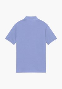 Ljust blå kortärmad polotröja med en strukturerad krage, tillverkad av textil med struktur, med rak nederkant och minimal design.