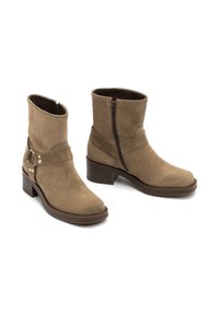 Botas de tobillo de ante marrón con cremallera lateral, detalle de correa envolvente y tacón cuadrado. Textura suave y diseño de punta redondeada.