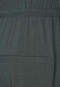 Tessuto verde scuro con una trama liscia, dotato di una vita elasticizzata e di una singola tasca posteriore con cuciture a vista.