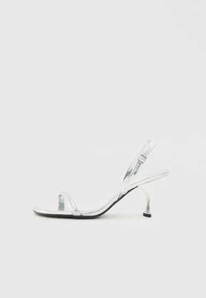 Sølv patentlæder slingback højhælede sandal med en smal tårem, justerbar spænde og en slank hæl.