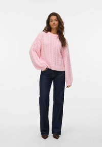 Un pull en maille torsadée rose clair avec une silhouette ample et un col rond, associé à un jean droit bleu foncé.