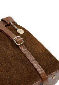 Bruine suède handtas met een gestructureerde leren schouderband, goudkleurige hardware en een decoratief metalen label. Vierkante vorm met gedetailleerde stiksels.