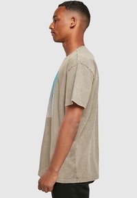 Lysbrun oversized T-shirt lavet af bomuld. Har et blåt bølgemønster på fronten og korte ærmer. Enkel rund halsudskæring.