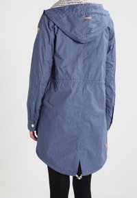 Blå huva jacka i texturerat tyg med åtstramad midja, långa ärmar och längre bakstycke. Har logotypdetalj på ärmen.