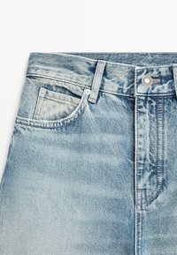 Lyseblå denimjeans med frontknaplukning, bæltestropper og en lille møntlomme inde i den højre forreste lomme.