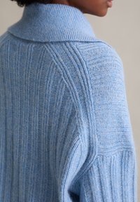 Hellblauer, gestrickter Pullover mit einer gerippten Textur und hohem Kragen. Verfügt über vertikale und horizontale Muster entlang des Stoffs.