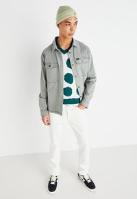 Gray denim jacket over a green and white polka dot sweater, paired with white jeans and black sneakers with green accents. Light green beanie.