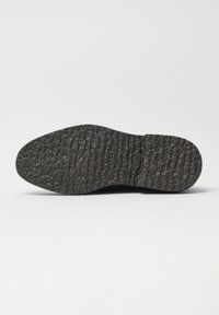 Czarna gumowa podeszwa buta z teksturowaną powierzchnią o nieregularnym wzorze i lekkim zakrzywieniu. Trwała i zaprojektowana dla lepszej przyczepności.