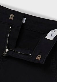 Svarta denimjeans med dragkedja, metallknapp och kontrasterande vit knappstängning; har en klassisk 5-fickdesign.