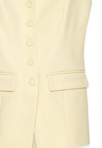 Kreem värvi kohandatud vest, kus on viis kangaga kaetud nupukest, nurgelise kraega ja kaks lamedat taskut. Vest paistab silma sujuva ja tekstuurse pinnaga.